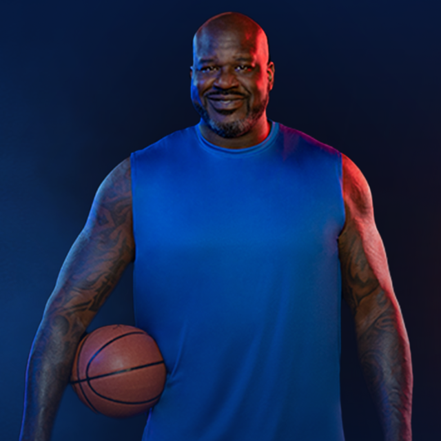 Shaquille O'Neil smiling as he holds a basket ball under his right arm.